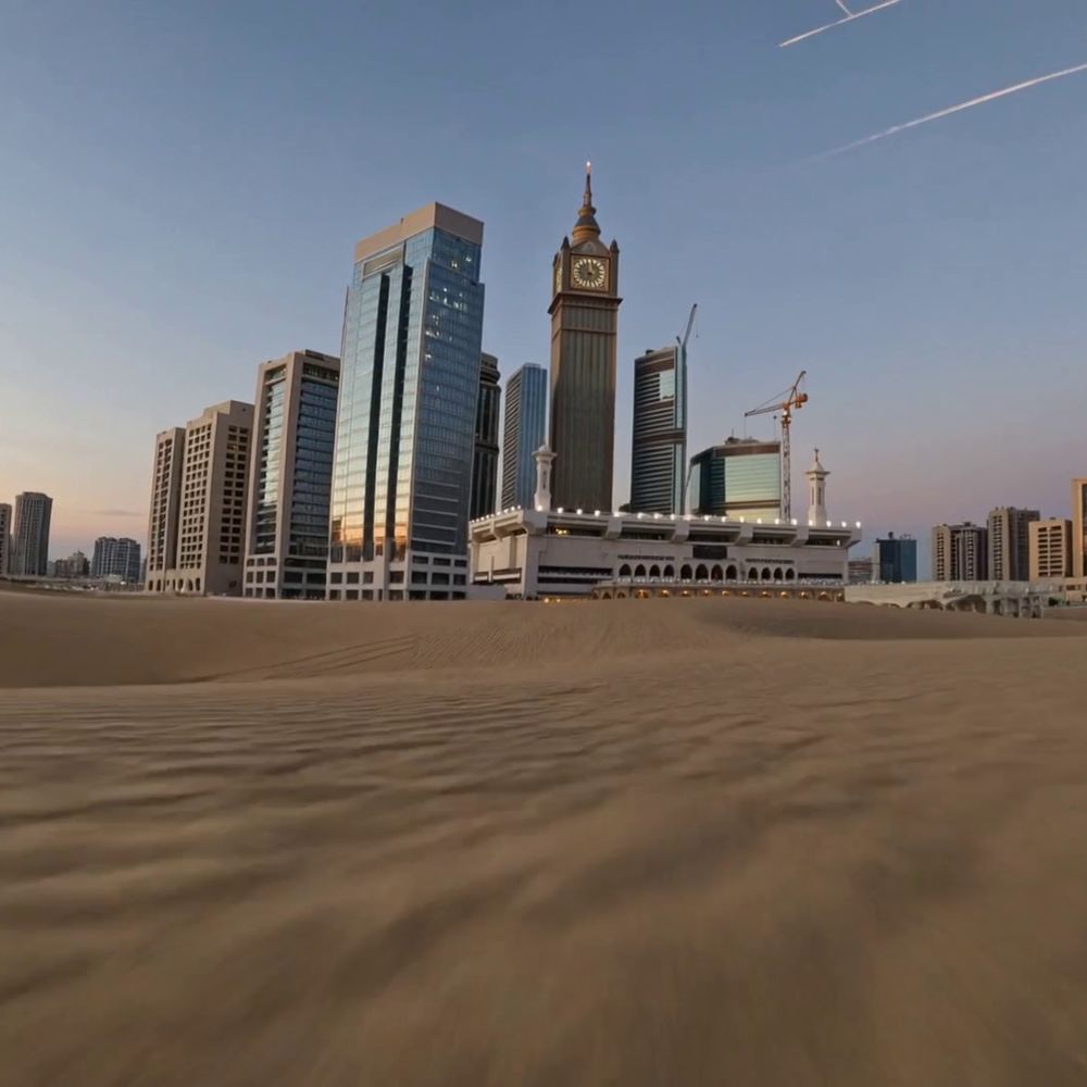 A modern skyline of glass towers and a clock tower, beyond the sand